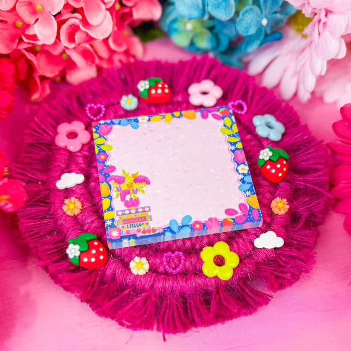 Sticky notes featuring a floral design with a book stack, and a border of vines and florals, on a pink backdrop.