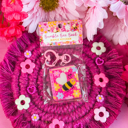 Pink decorative keychain with a bee-theme, surrounded by pink flowers.