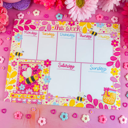 Weekly planner with bee design on a pink background with flowers and decorative elements.
