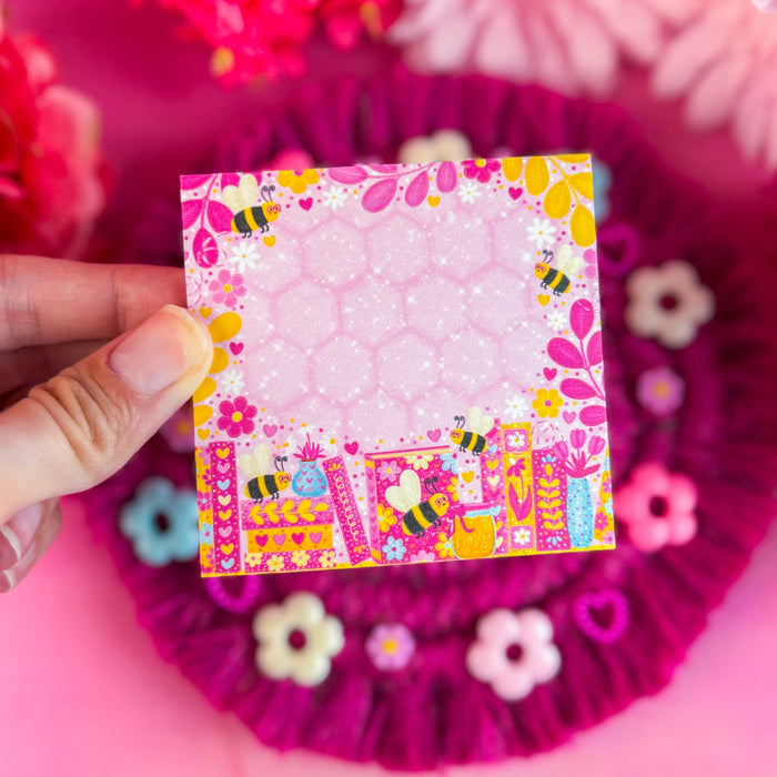 Colorful sticky notes with floral and bee design held over pink flowers