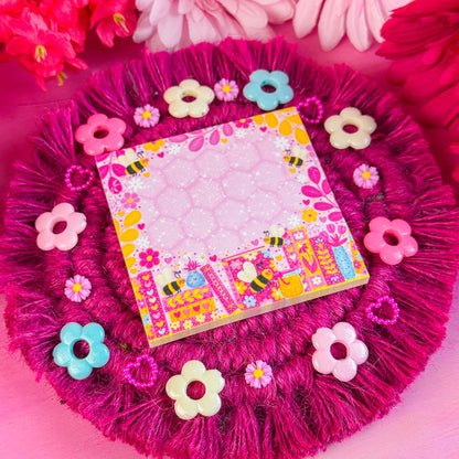 Colorful notepad with floral decorations on a pink textured surface with flowers.