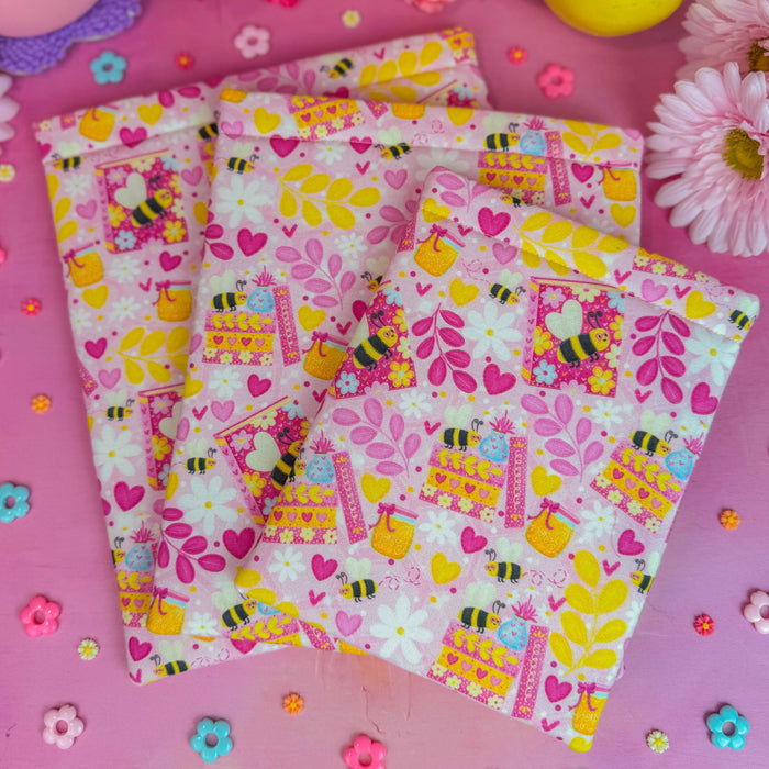 Colorful book sleeve with bee and flower patterns on a pink background with flowers.
