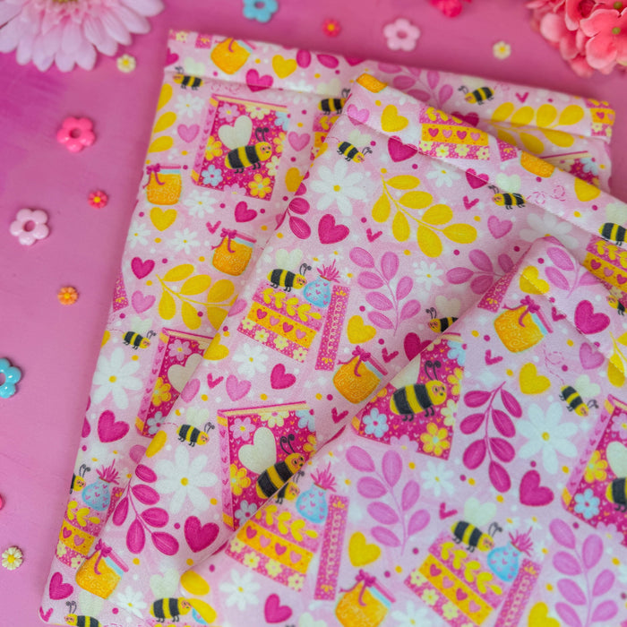 Colorful fabric with bee and heart pattern on a pink background with flowers.
