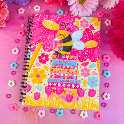 Notebook with a bee illustration on a pink background with flowers