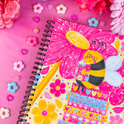 Colorful notebook with a bee illustration on a pink background with flowers and toys.