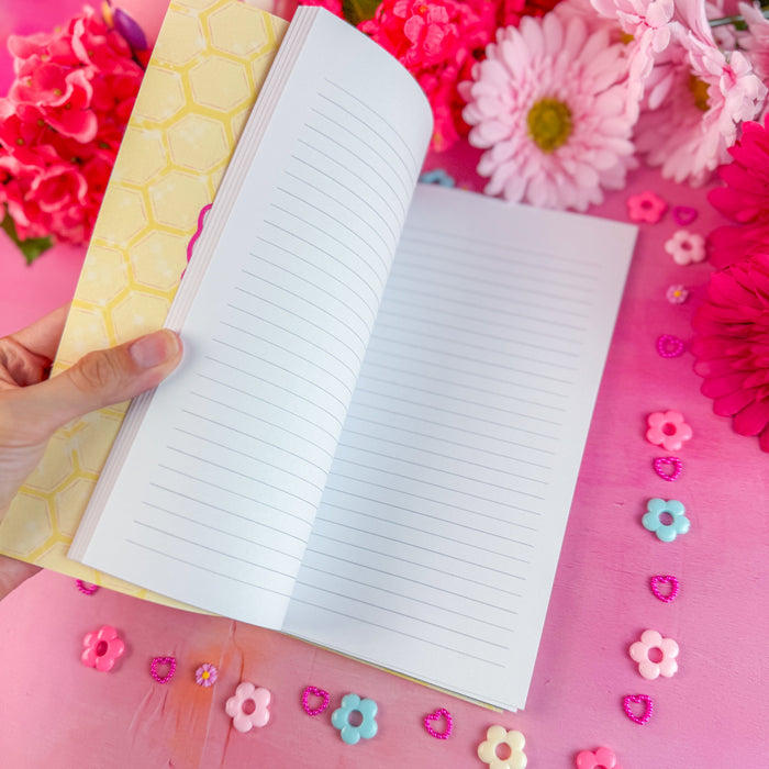 Open notebook held over a pink surface with flowers and decorative elements