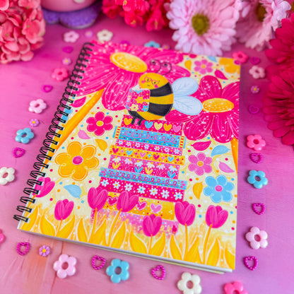 Colorful notebook with a bee design on a pink background with flowers and decorative elements.