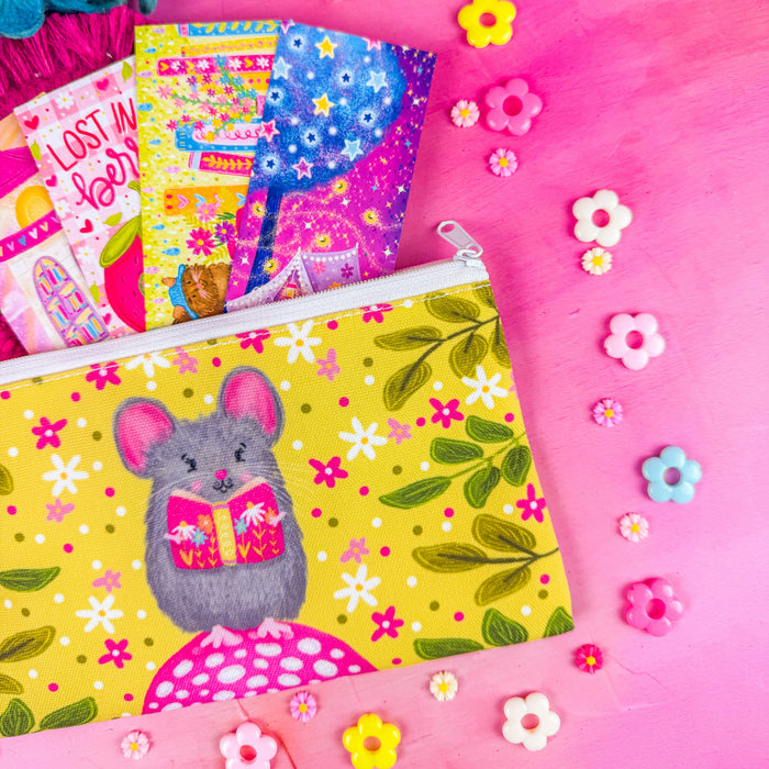 A close up of the white zippered fabric pouch. The pattern on the pouch features a mouse holding a pink book against a chartreuse background decorated with pink and white flowers and green leaves.