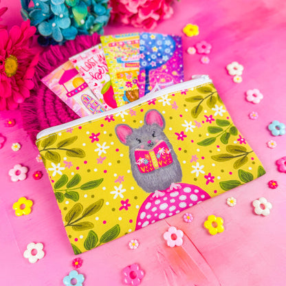 A white zippered fabric pouch. The pattern on the pouch features a mouse holding a pink book against a chartreuse background decorated with pink and white flowers and green leaves.