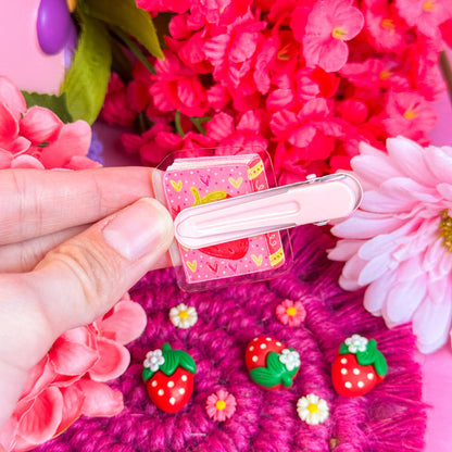 Backside of an acrylic hair clip held by a hand against a pink floral background