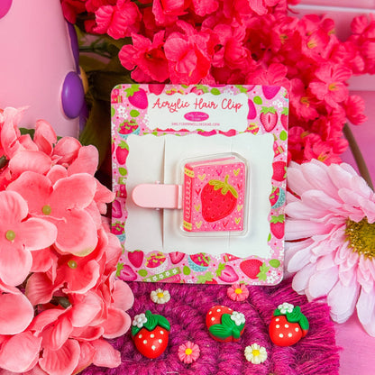 Strawberry-themed hair clip in packaging with pink flowers in the background