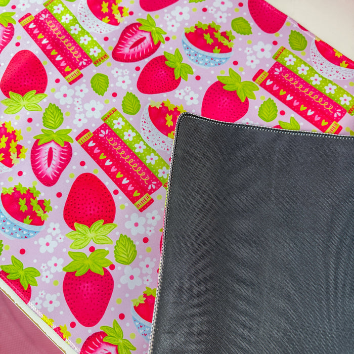 A pink and white strawberry-themed desk mat on a white desk, styled with a matching pink computer mousepad, a pink monitor, and various cute desk accessories.