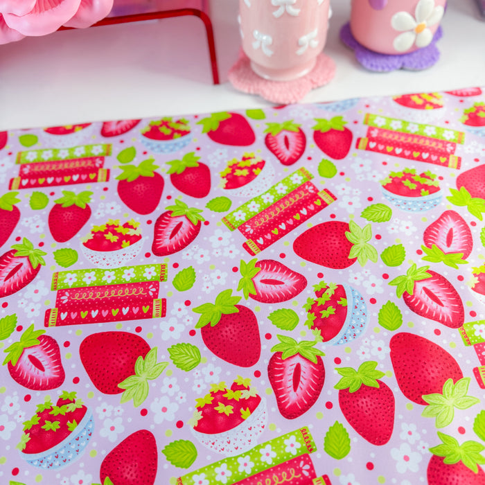 A pink and white strawberry-themed desk mat on a white desk, styled with a matching pink computer mousepad, a pink monitor, and various cute desk accessories.