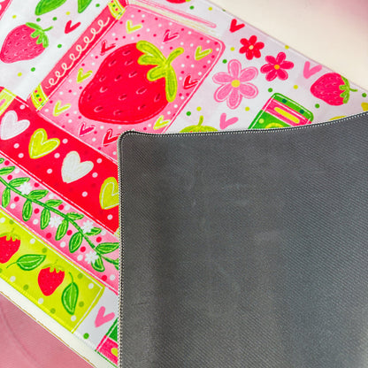 A close-up of a dark gray textured mousepad partially covering a colorful printed mousepad with strawberry and floral patterns.