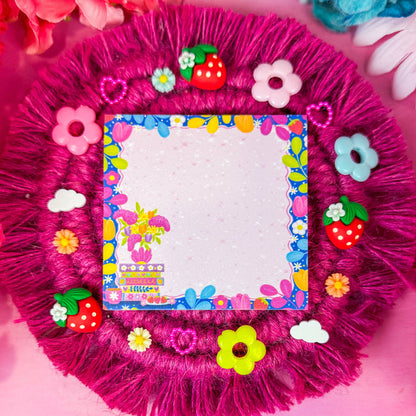 Sticky notes featuring a floral design with a book stack, and a border of vines and florals, on a pink backdrop.